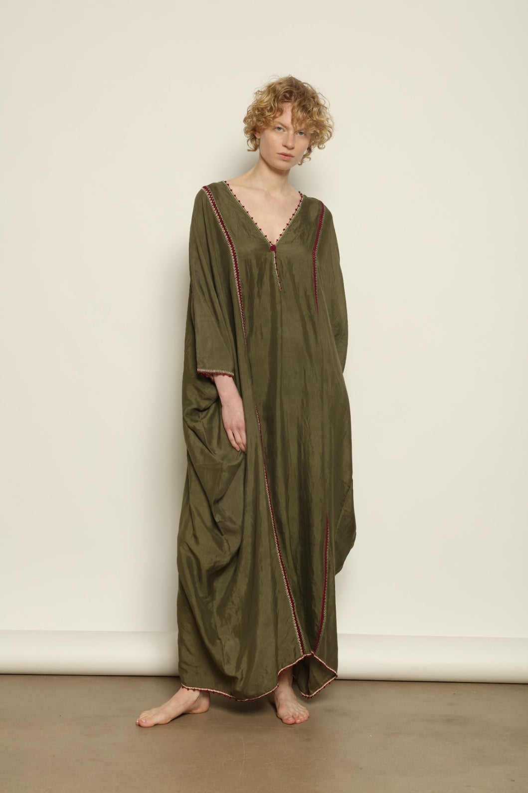 Model is wearing the Thea Olive Silk Dress by Supernaturae in soft olive-toned handwoven silk from Murshidabad, featuring a relaxed flowing silhouette and elegant open back. This sustainable ethical fashion dress is crafted using traditional weaving techniques and natural fibers, designed for everyday wear with a breathable, lightweight drape.