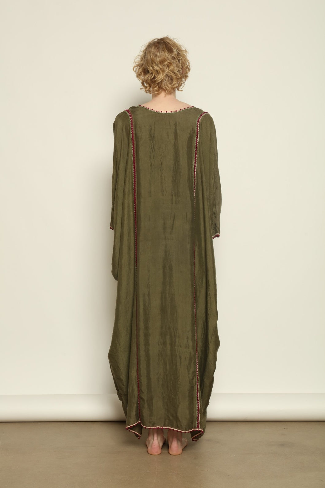 Model is wearing the Thea Olive Silk Dress by Supernaturae in soft olive-toned handwoven silk from Murshidabad, featuring a relaxed flowing silhouette and elegant open back. This sustainable ethical fashion dress is crafted using traditional weaving techniques and natural fibers, designed for everyday wear with a breathable, lightweight drape.