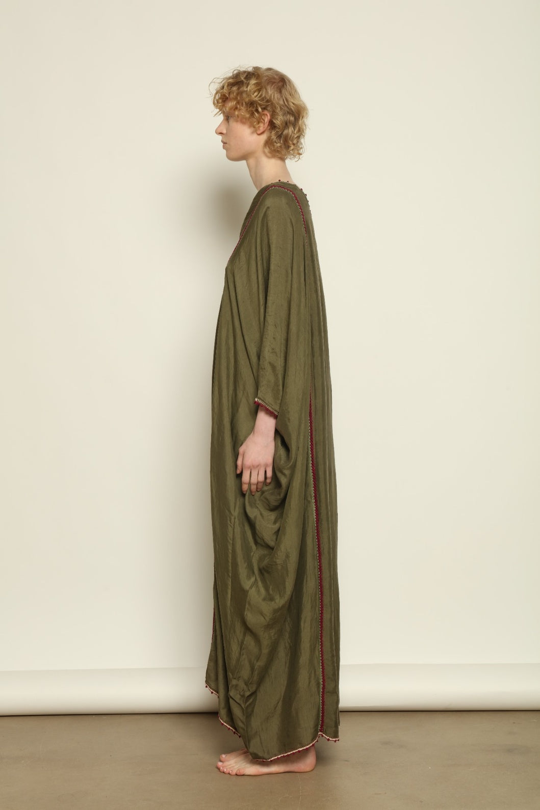 Model is wearing the Thea Olive Silk Dress by Supernaturae in soft olive-toned handwoven silk from Murshidabad, featuring a relaxed flowing silhouette and elegant open back. This sustainable ethical fashion dress is crafted using traditional weaving techniques and natural fibers, designed for everyday wear with a breathable, lightweight drape.