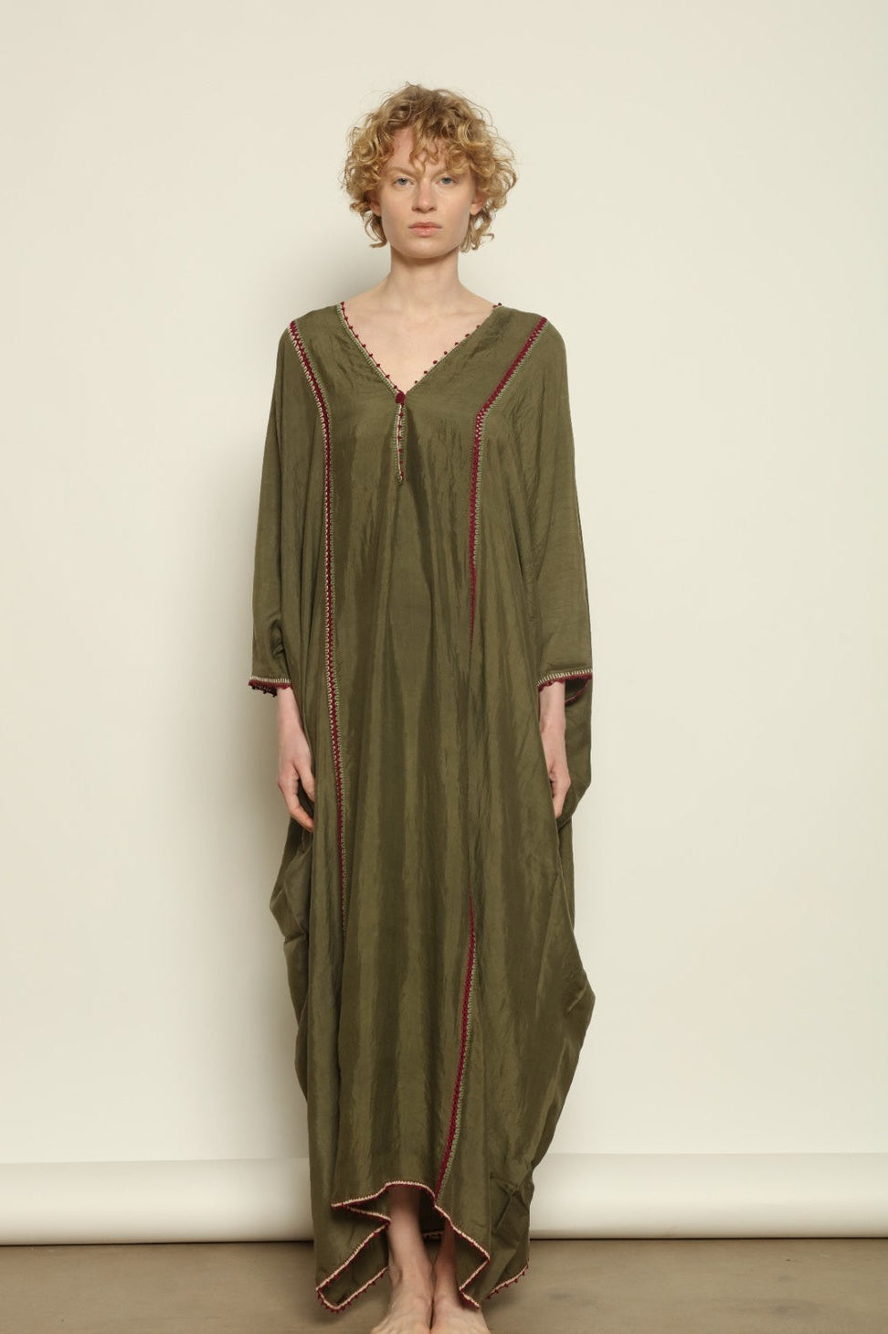 Model is wearing the Thea Olive Silk Dress by Supernaturae in soft olive-toned handwoven silk from Murshidabad, featuring a relaxed flowing silhouette and elegant open back. This sustainable ethical fashion dress is crafted using traditional weaving techniques and natural fibers, designed for everyday wear with a breathable, lightweight drape.