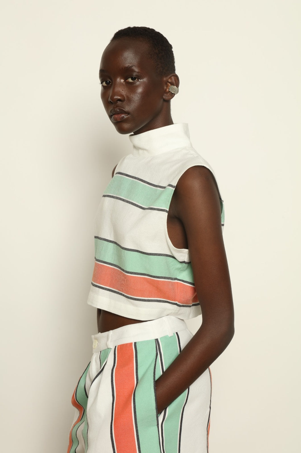 Model is wearing The Cropped Turtleneck by Marrakshi Life, part of House of Nomad Stories collection, handwoven artisanal cotton top with boxy architectural silhouette, high turtleneck, and breathable weave
