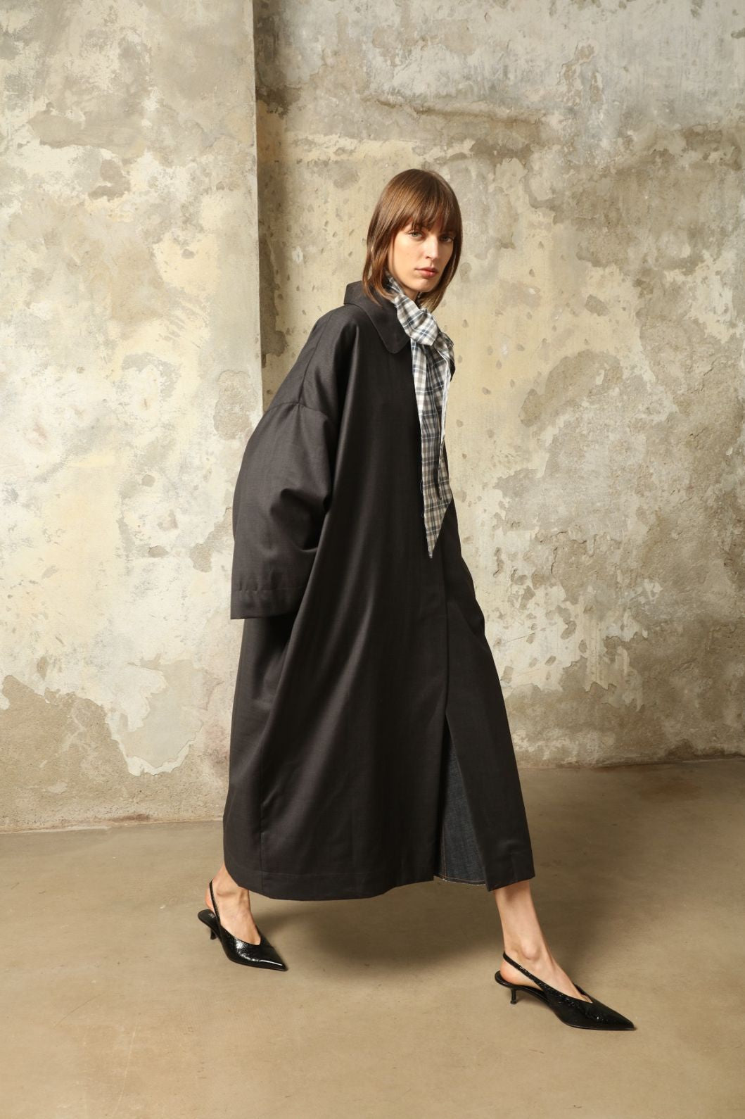 Model is wearing the Tiflis Anthracite Coat in Cool Wool by House of Woven Stories – structured yet fluid silhouette with kimono-inspired sleeves, Peter Pan collar, vintage button, and natural silk lining.