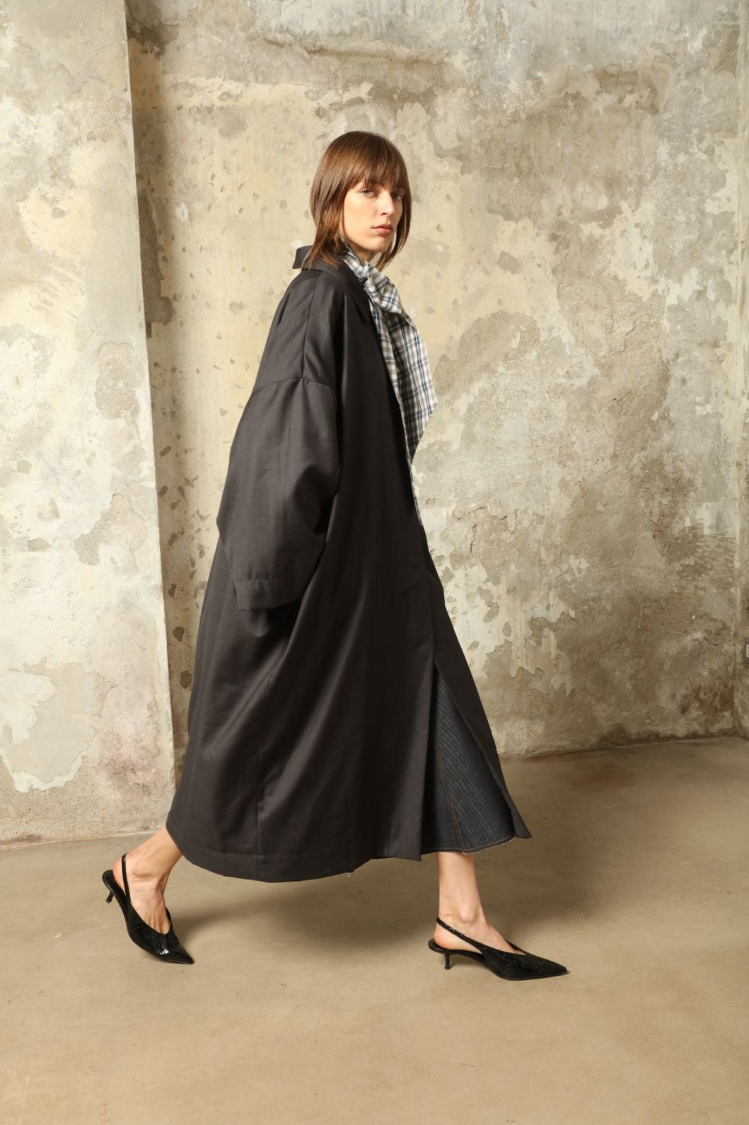 Model is wearing the Tiflis Anthracite Coat in Cool Wool by House of Woven Stories – structured yet fluid silhouette with kimono-inspired sleeves, Peter Pan collar, vintage button, and natural silk lining.