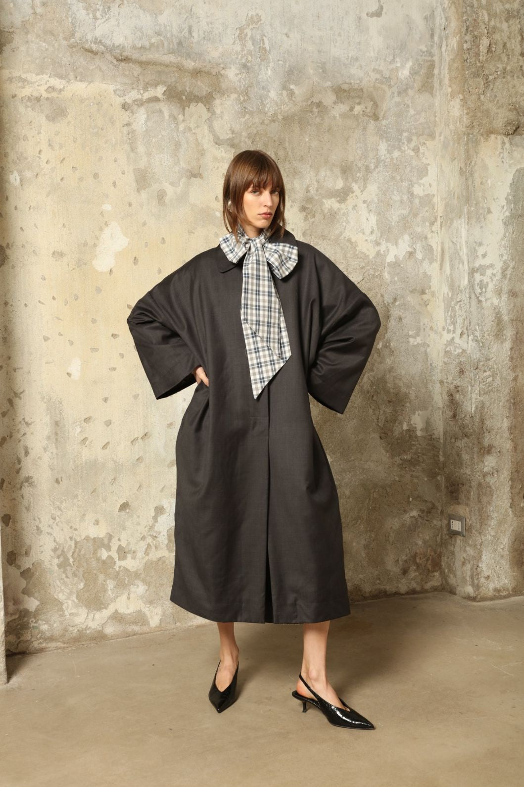 Model is wearing the Tiflis Anthracite Coat in Cool Wool by House of Woven Stories – structured yet fluid silhouette with kimono-inspired sleeves, Peter Pan collar, vintage button, and natural silk lining.