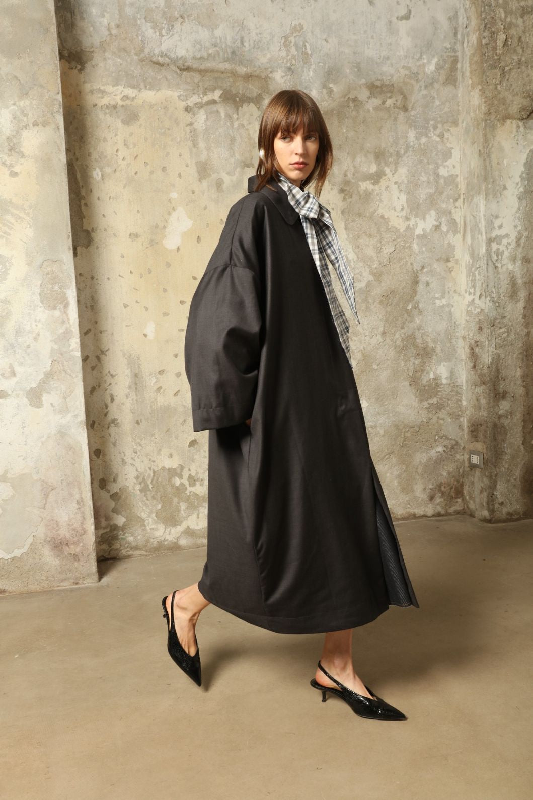 Model is wearing the Tiflis Anthracite Coat in Cool Wool by House of Woven Stories – structured yet fluid silhouette with kimono-inspired sleeves, Peter Pan collar, vintage button, and natural silk lining.