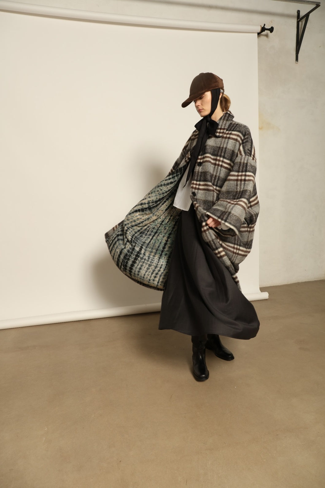 Model is wearing the Tiflis Checked Coat by House of Woven Stories, crafted from a soft wool blend with muted grey and brown checks, featuring an oversized silhouette, wide sleeves, and structured collar for timeless elegance.