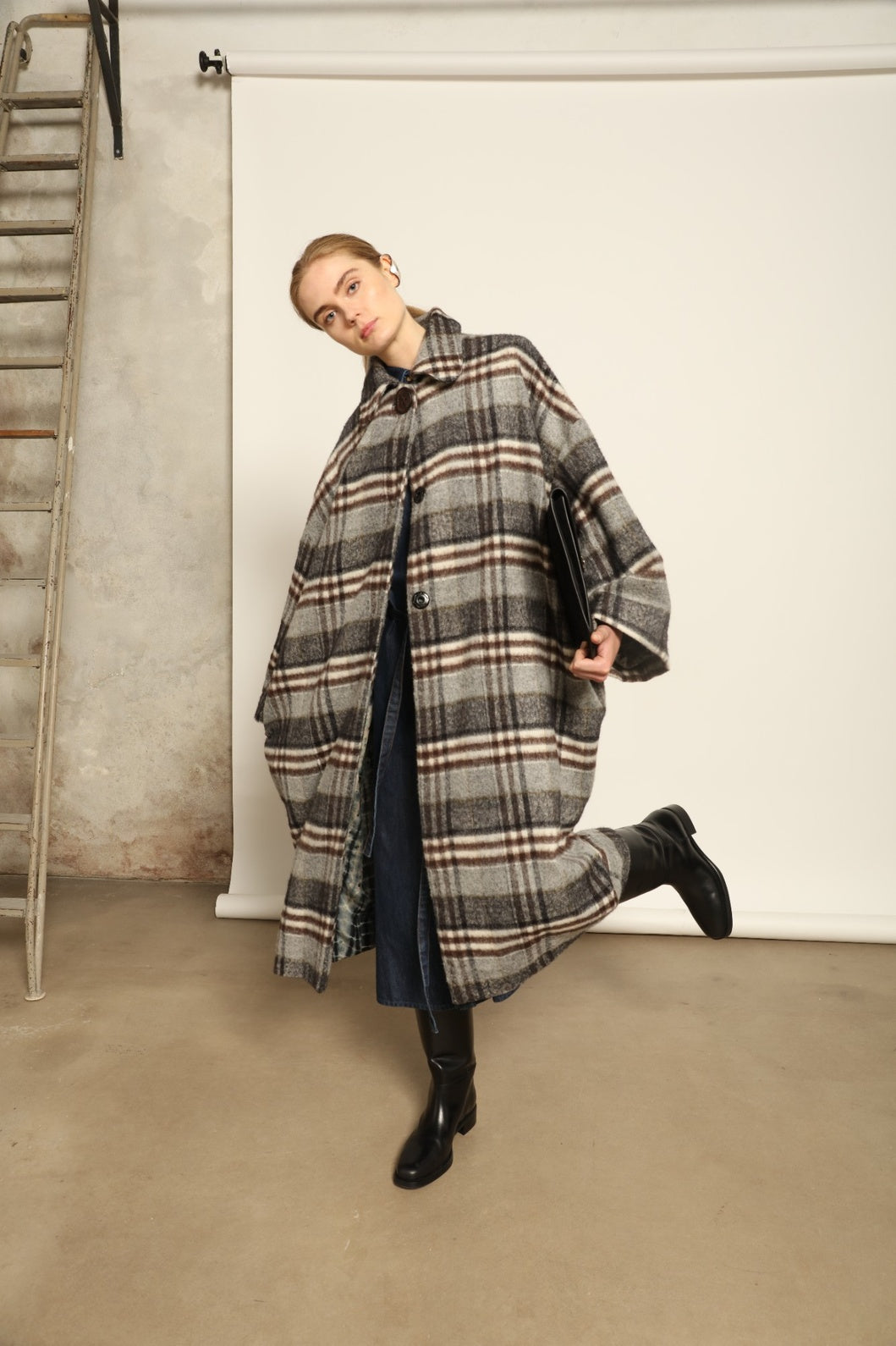 Model is wearing the Tiflis Checked Coat by House of Woven Stories, crafted from a soft wool blend with muted grey and brown checks, featuring an oversized silhouette, wide sleeves, and structured collar for timeless elegance.