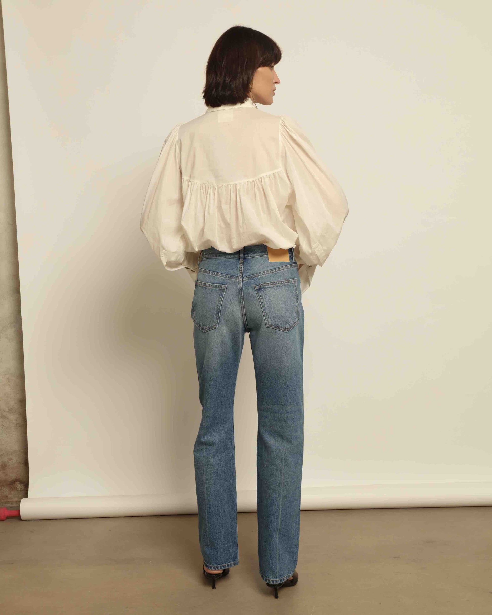 Model is wearing the Tilda Mid-Rise Draped Straight Jean by B Sides in classic indigo denim, mid-rise fit with straight tapered leg and curved inseam for a leg-lengthening silhouette.
