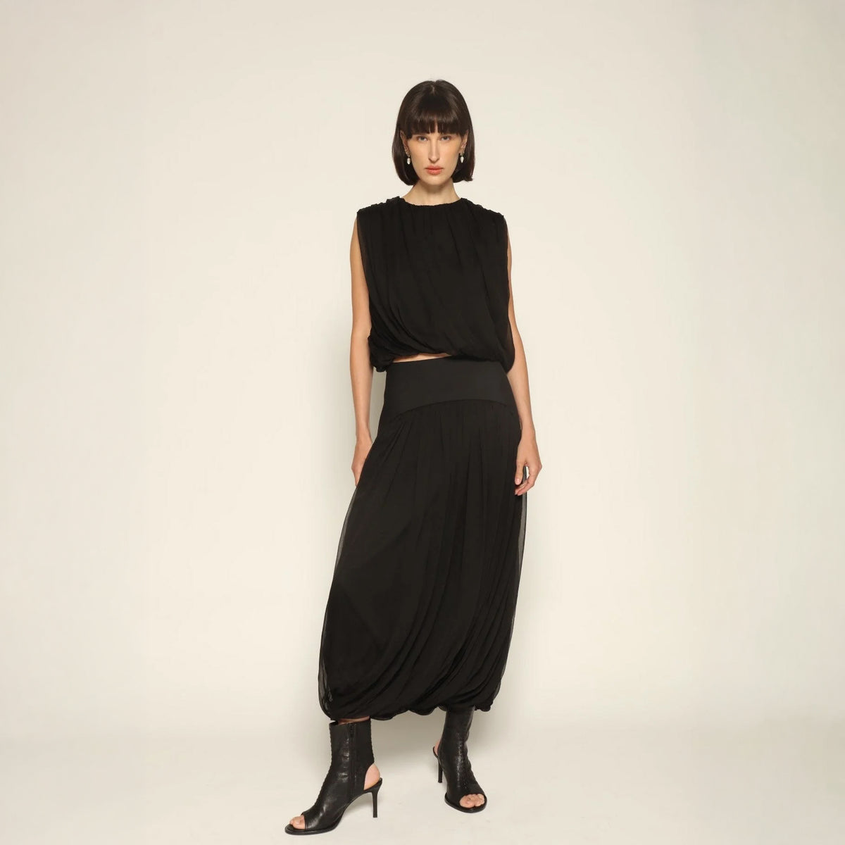 Model wearing the Twisted Suri Skirt in Black by Abadia from the House of Nomad Stories collection, featuring a curved waistband, mid-waist fit, and an elegant draped silhouette with fluid movement.