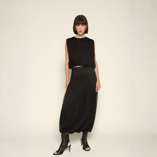 Model wearing the Twisted Suri Skirt in Black by Abadia from the House of Nomad Stories collection, featuring a curved waistband, mid-waist fit, and an elegant draped silhouette with fluid movement.