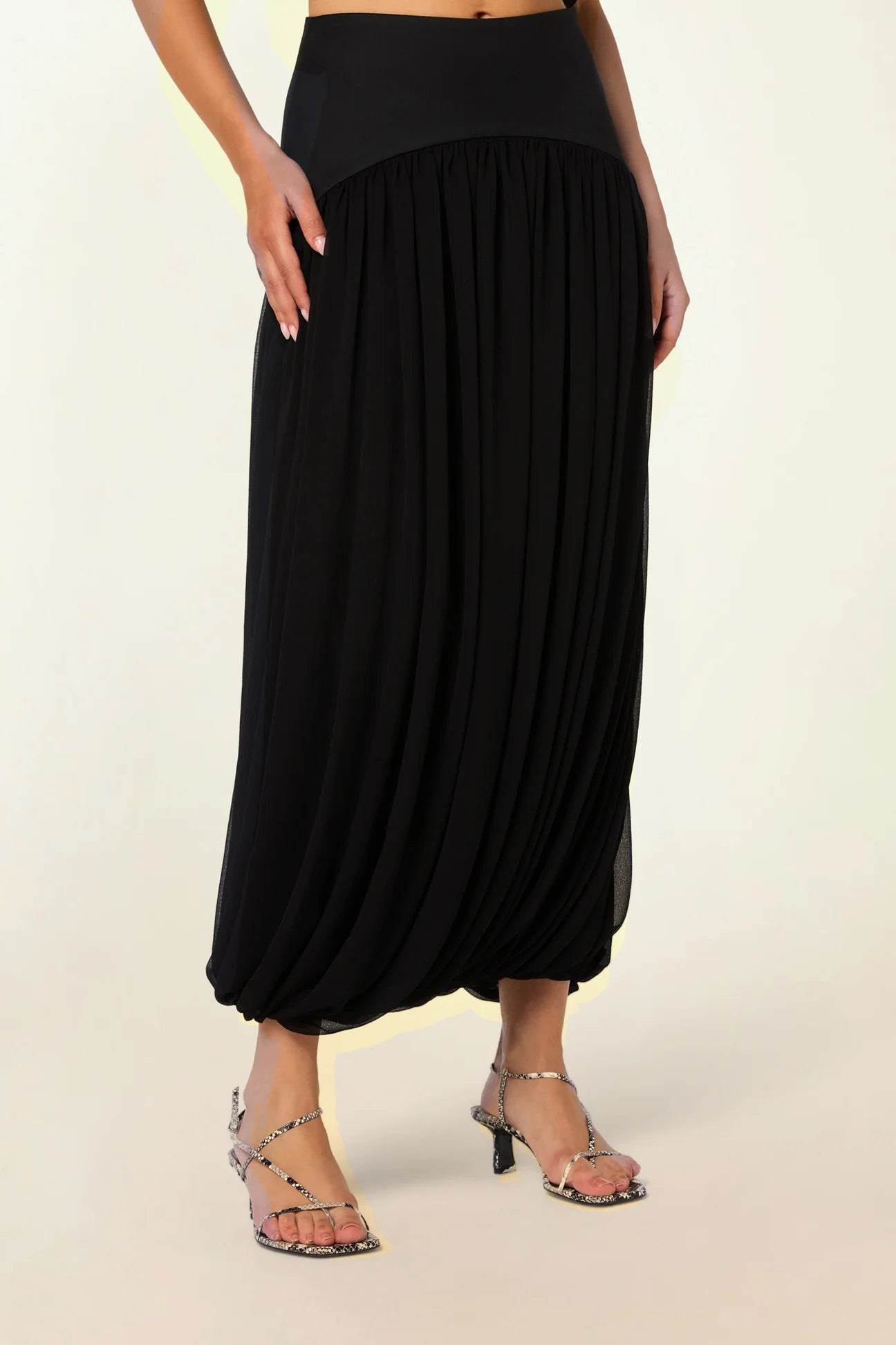 Model wearing the Twisted Suri Skirt in Black by Abadia from the House of Nomad Stories collection, featuring a curved waistband, mid-waist fit, and an elegant draped silhouette with fluid movement.