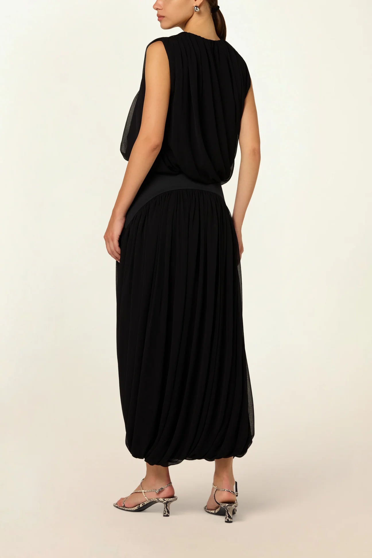Model wearing the Twisted Suri Skirt in Black by Abadia from the House of Nomad Stories collection, featuring a curved waistband, mid-waist fit, and an elegant draped silhouette with fluid movement.