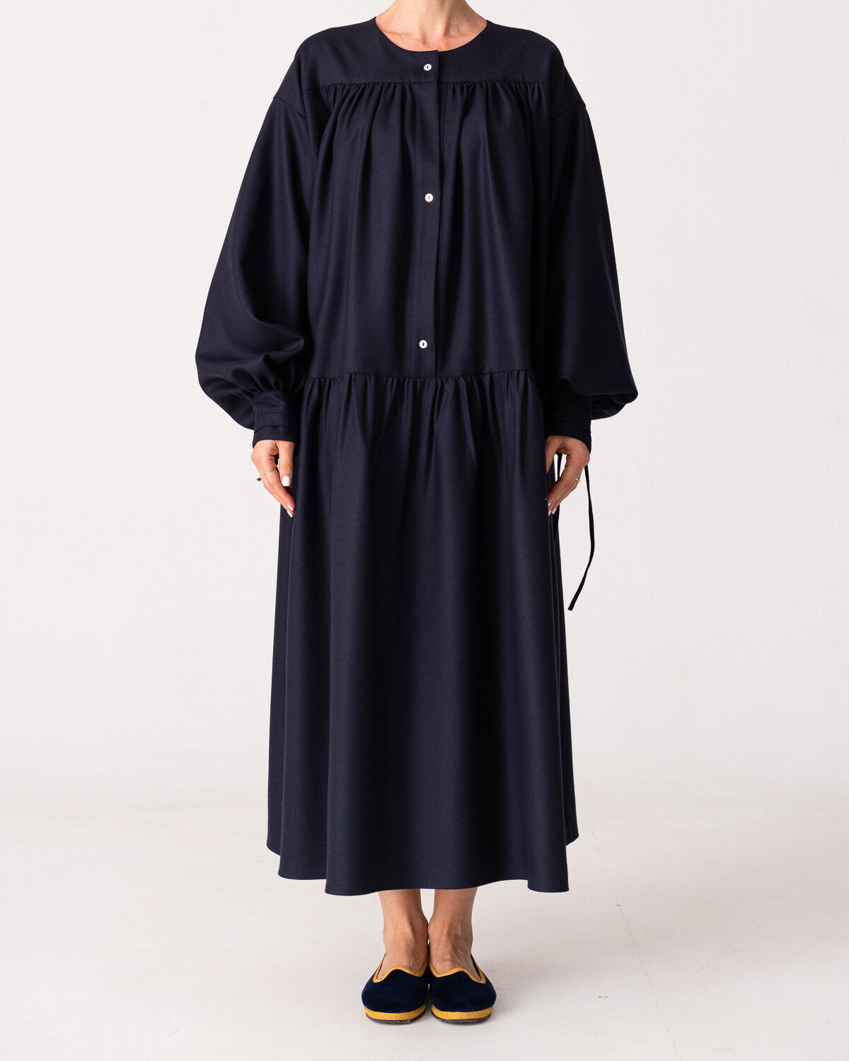 Model is wearing the Winter Calla Dress by Les Vacances d’Irina, a full-length navy merino wool dress with drop-waist silhouette, billowy sleeves, and bow cuffs, handmade in Bucharest and available at House of Woven Stories.