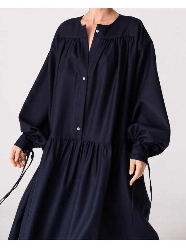 Model is wearing the Winter Calla Dress by Les Vacances d’Irina, a full-length navy merino wool dress with drop-waist silhouette, billowy sleeves, and bow cuffs, handmade in Bucharest and available at House of Woven Stories.