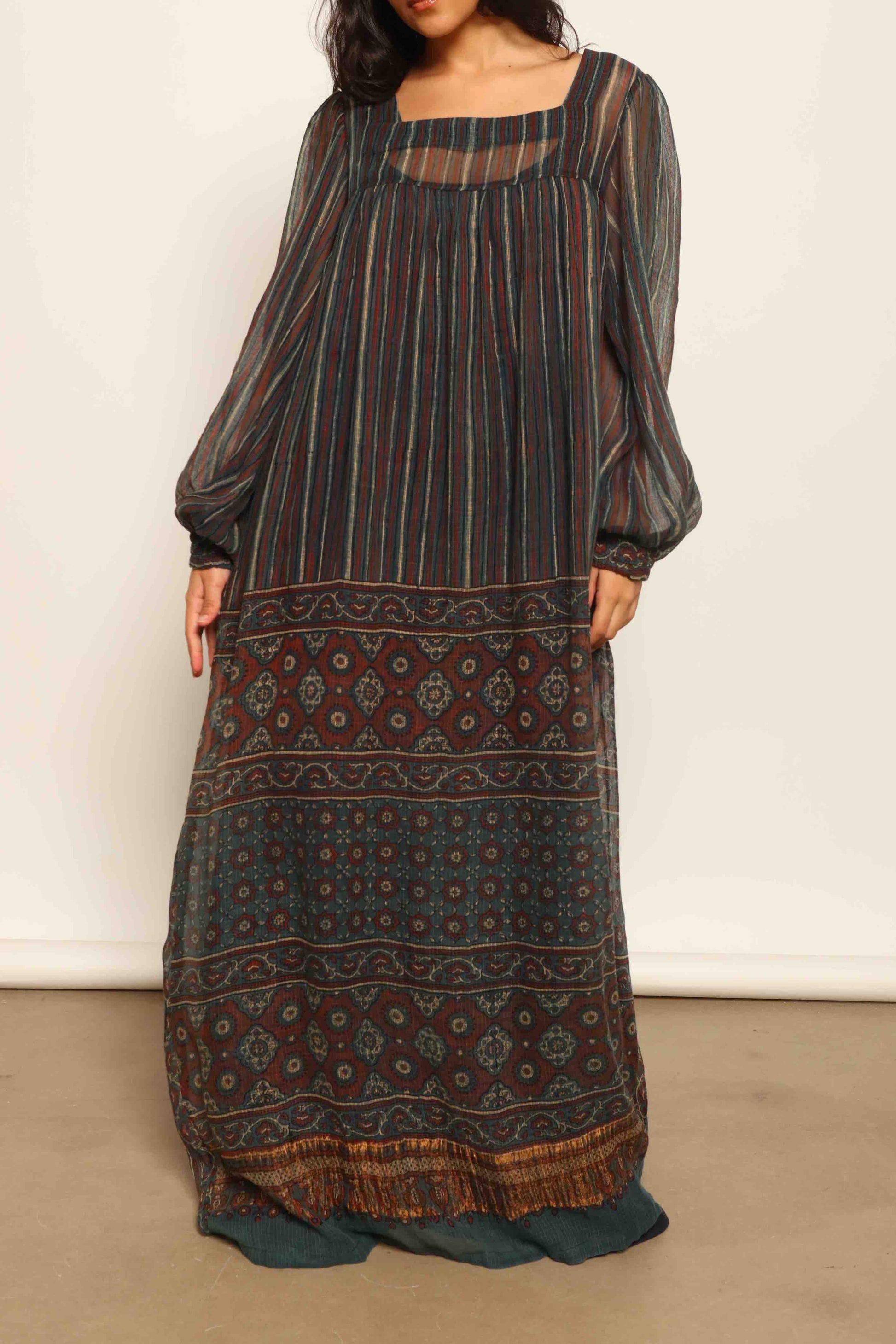 Model is wearing the Woodstock Dark silk dress by House Of Woven Stories, handcrafted in Italy from re-wearable sari fabric, featuring sheer sleeves, handprinted details, and a flowing silhouette.
