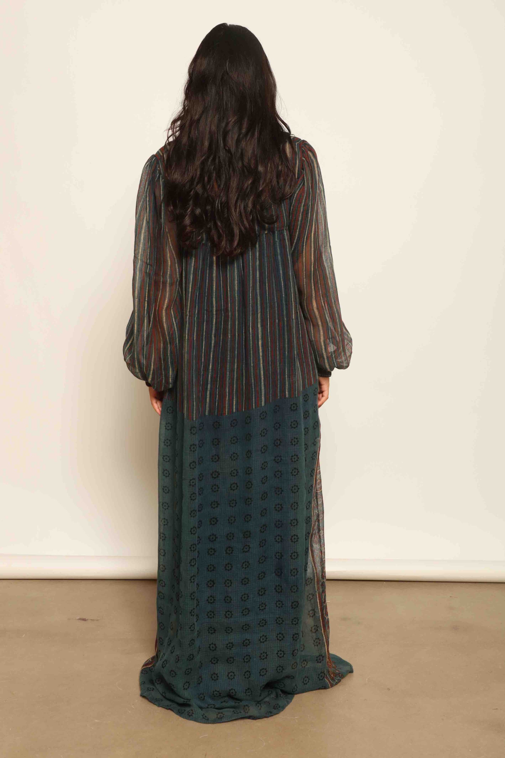 Model is wearing the Woodstock Dark silk dress by House Of Woven Stories, handcrafted in Italy from re-wearable sari fabric, featuring sheer sleeves, handprinted details, and a flowing silhouette.