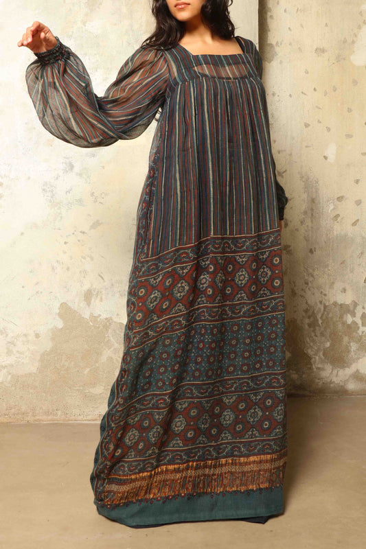 Model is wearing the Woodstock Dark silk dress by House Of Woven Stories, handcrafted in Italy from re-wearable sari fabric, featuring sheer sleeves, handprinted details, and a flowing silhouette.