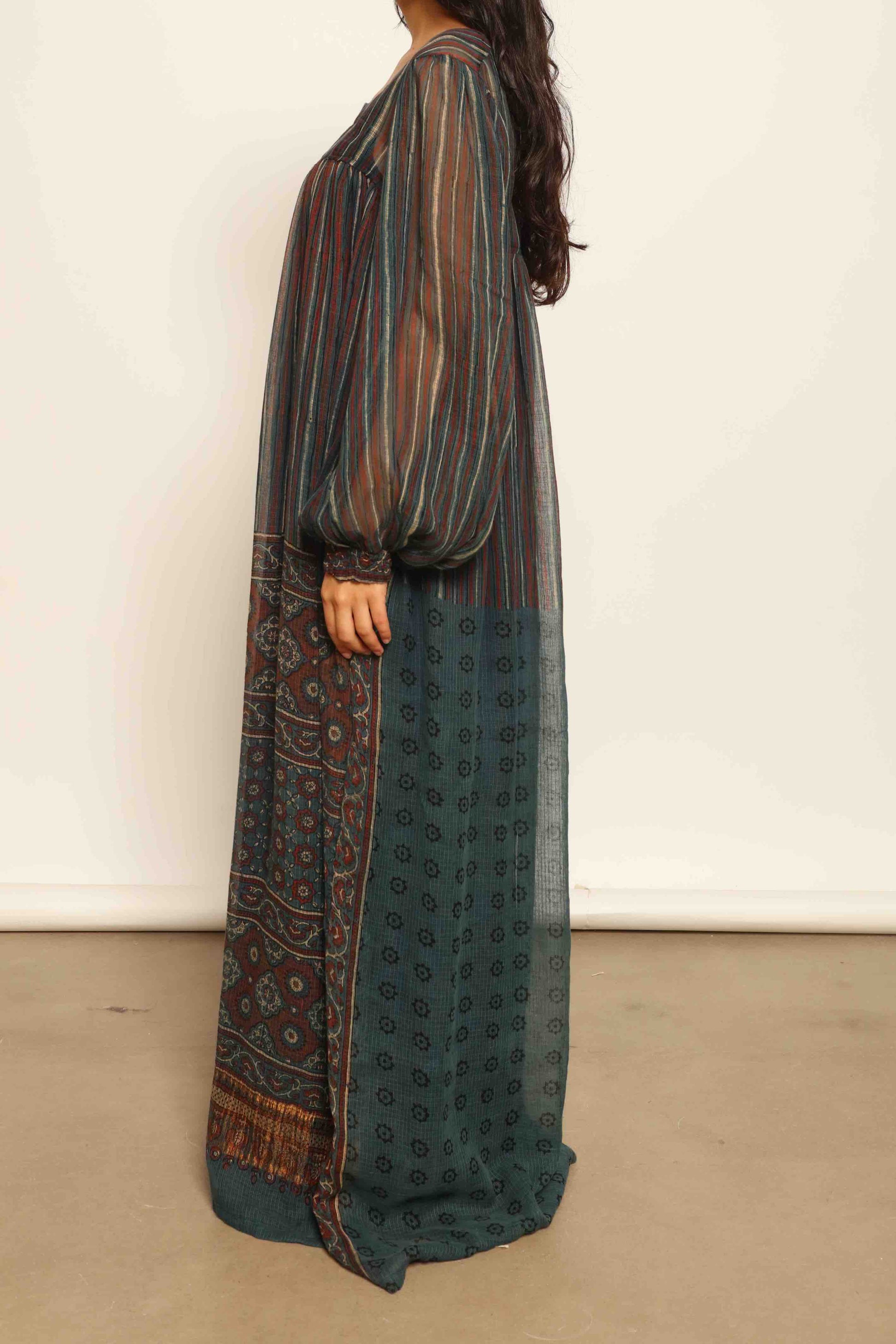 Model is wearing the Woodstock Dark silk dress by House Of Woven Stories, handcrafted in Italy from re-wearable sari fabric, featuring sheer sleeves, handprinted details, and a flowing silhouette.