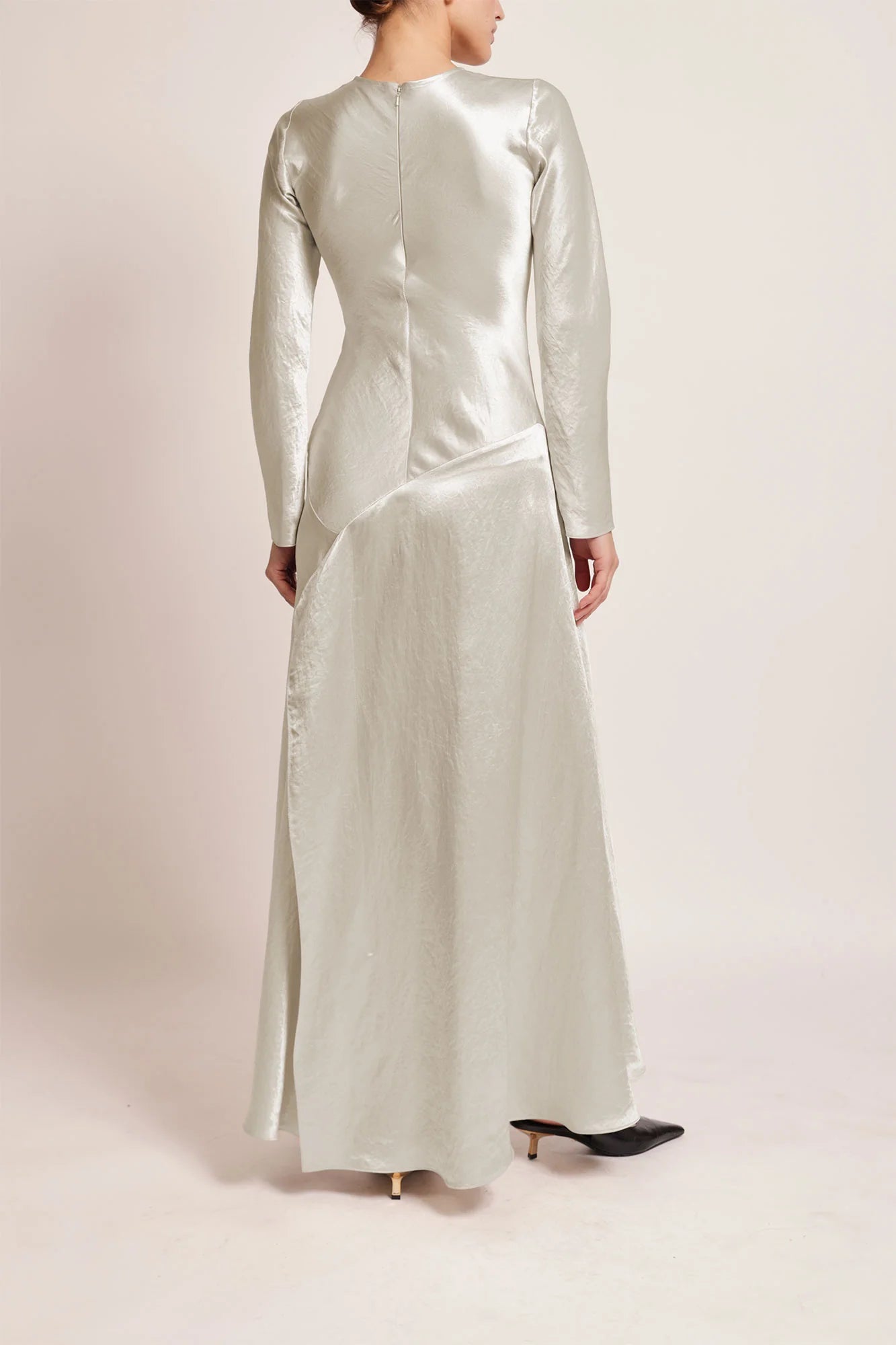 Model wearing a silver silk satin Yara Dress by Abadia from the House of Nomad Stories collection, featuring a bias-cut silhouette, long sleeves, and a fluid elegant drape with a subtle metallic sheen.