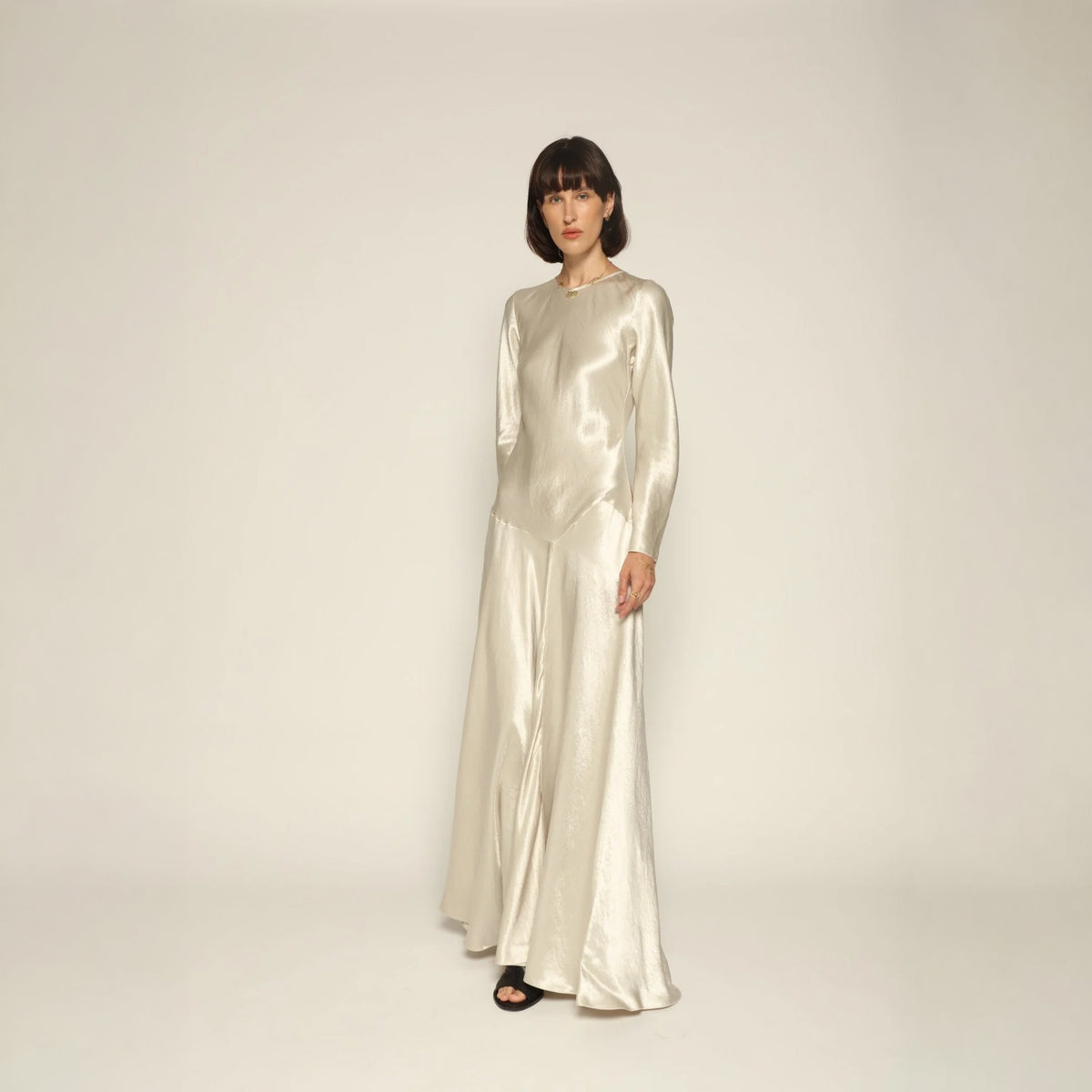 Model wearing a silver silk satin Yara Dress by Abadia from the House of Nomad Stories collection, featuring a bias-cut silhouette, long sleeves, and a fluid elegant drape with a subtle metallic sheen.