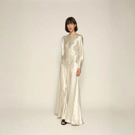 Model wearing a silver silk satin Yara Dress by Abadia from the House of Nomad Stories collection, featuring a bias-cut silhouette, long sleeves, and a fluid elegant drape with a subtle metallic sheen.