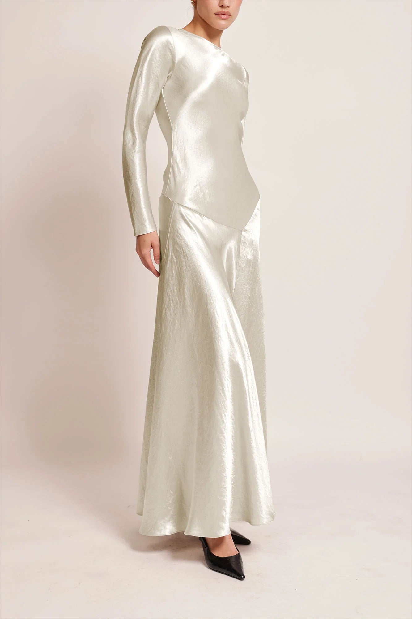 Model wearing a silver silk satin Yara Dress by Abadia from the House of Nomad Stories collection, featuring a bias-cut silhouette, long sleeves, and a fluid elegant drape with a subtle metallic sheen.